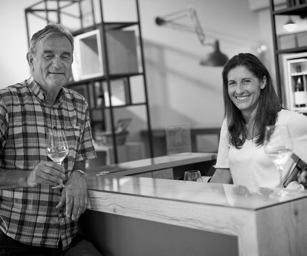 Schwarzweißfoto von zwei Winzern an einer modernen Verkostungstheke mit Weißweingläsern in der Hand