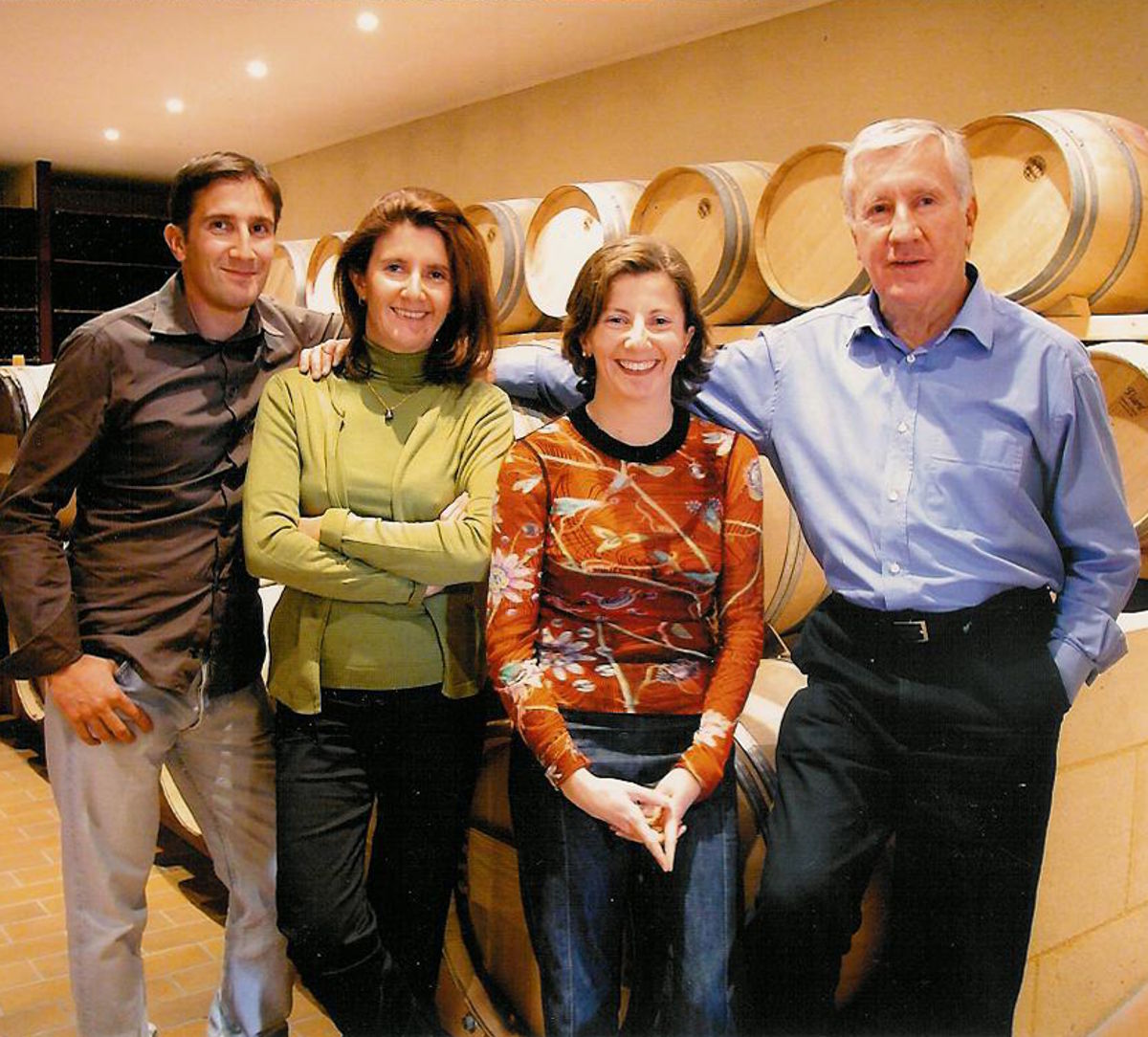 Vierköpfige Winzerfamilie steht lächelnd vor Barriquefässern in einem modernen Weinkeller.