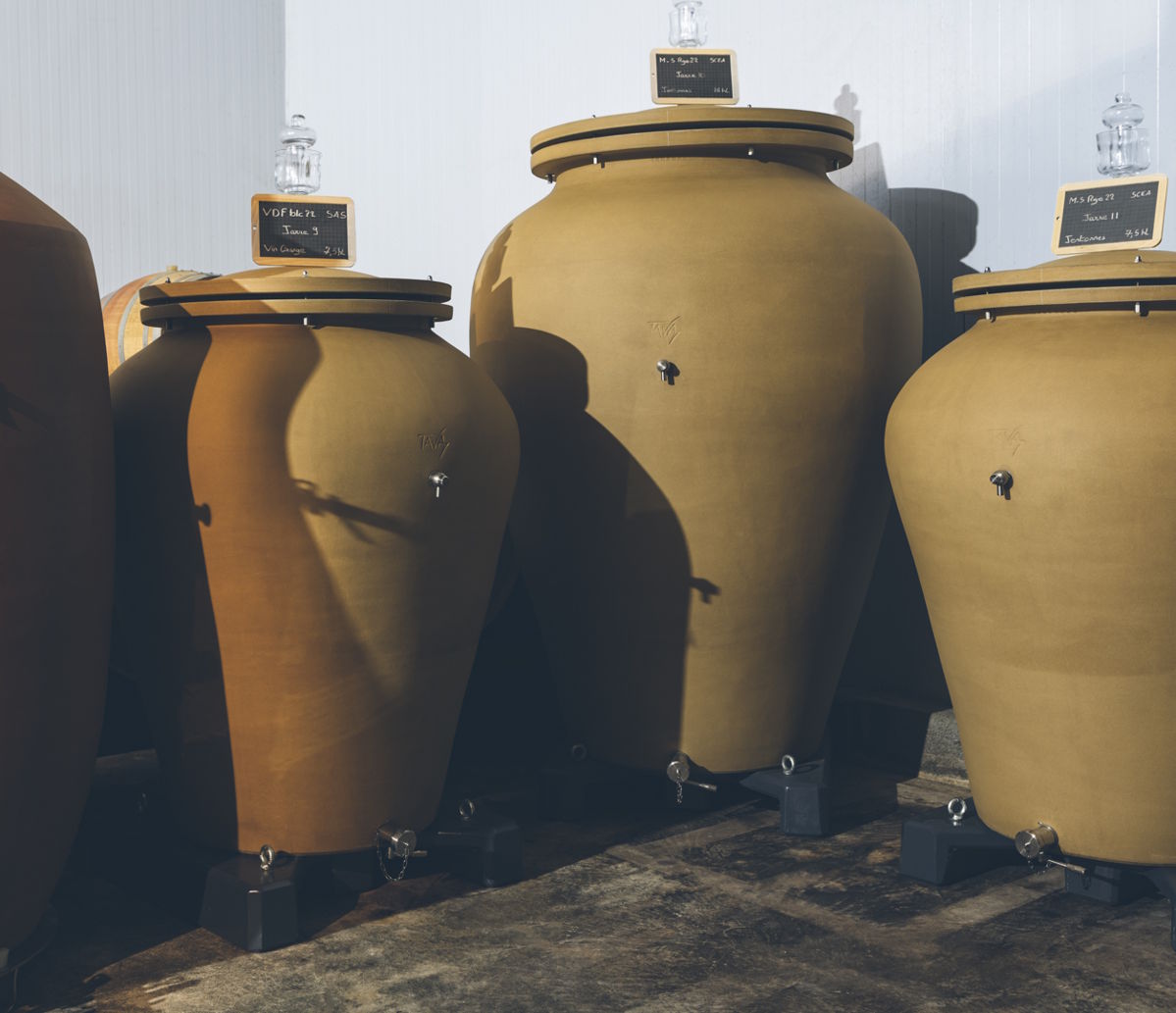 Mehrere große Tonamphoren zur Weinreifung in einem modernen Keller, jeweils mit Deckel und Beschriftung.