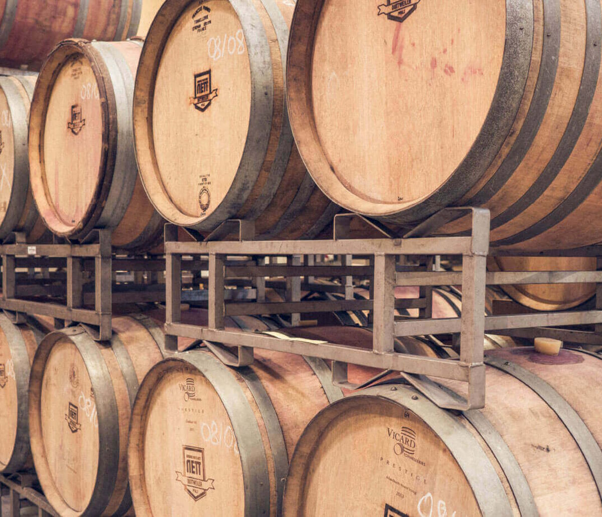 Gestapelte Holzfässer in einem Fasslager, mit Branding und Markierungen auf den Fassdeckeln.