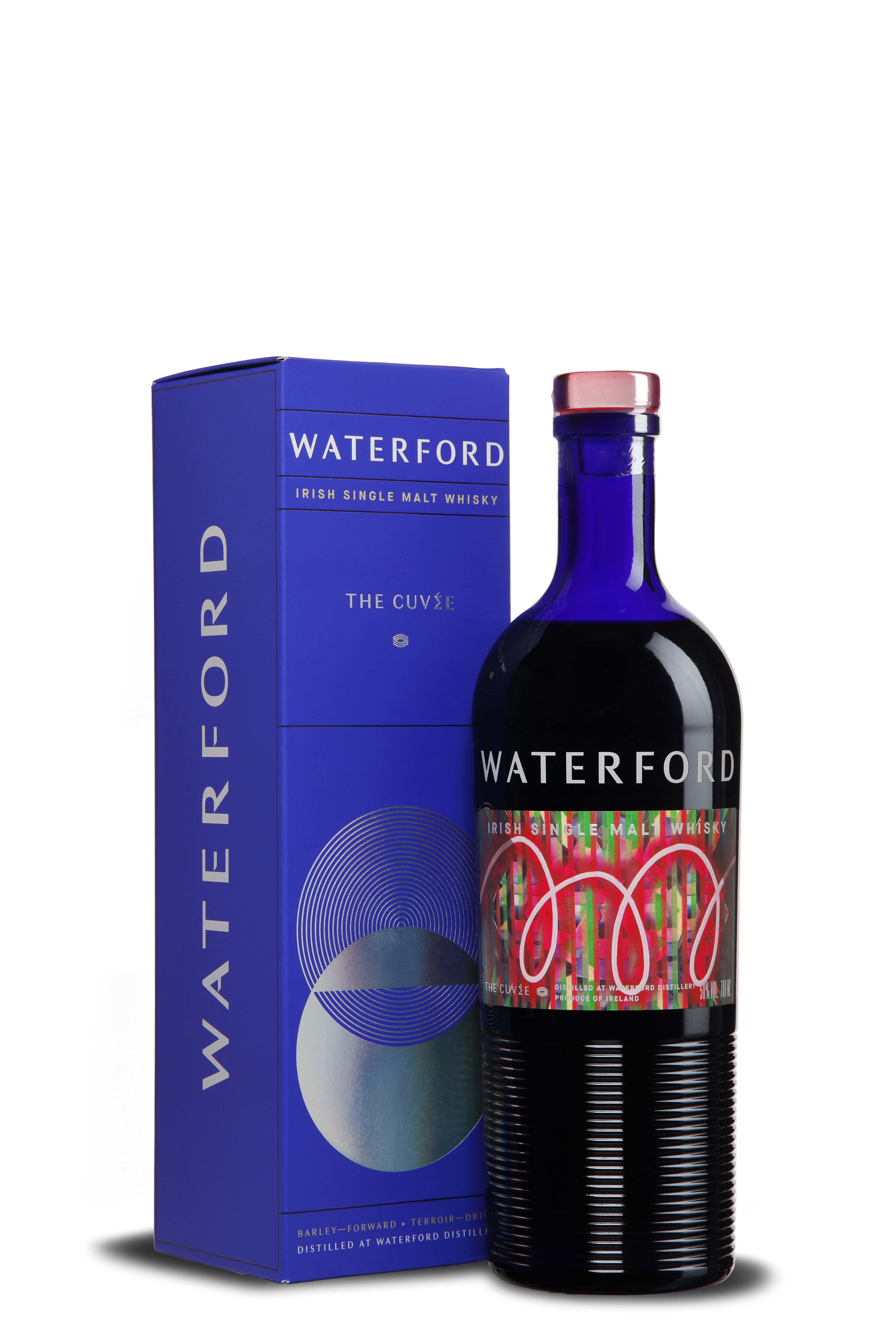 Flasche Waterford Irish Single Malt Whisky The Cuvée mit dunkelblauem Hals und goldfarbenem Kapselverschluss. Flasche ist dunkel und hat ein farbenfrohes Etikett mit roten und grünen Mustern. Daneben steht eine Verpackung mit Silber- und Blautönen.