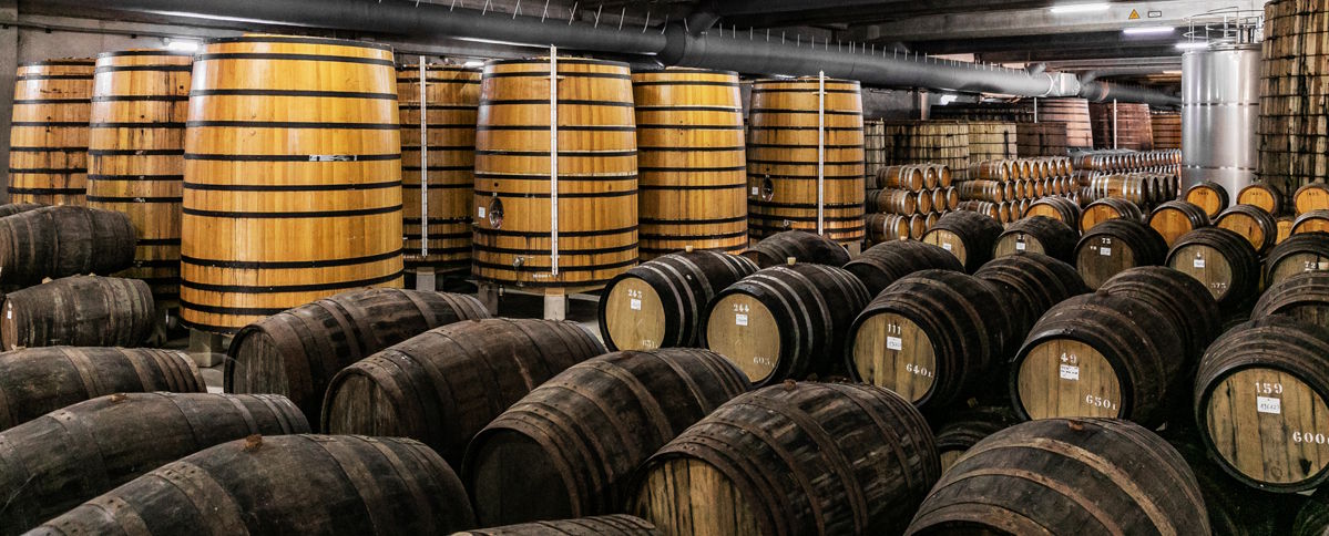 Lagerraum mit zahlreichen großen Holzfässern in unterschiedlichen Größen und Altersstufen, gestapelt und freistehend.