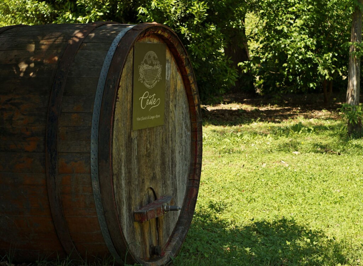  Großes, stehendes Holzfass mit Beschriftung im Grünen, umgeben von Bäumen und Rasen, vermutlich als Dekoration vor einem Weingut