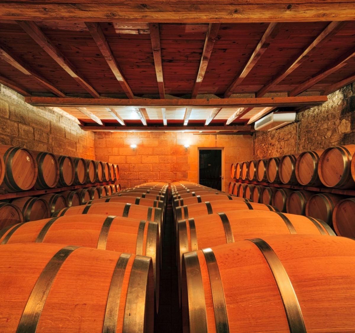 Stimmungsvoll beleuchteter Barriquekeller mit Reihen neuer Eichenfässer unter einem Holzbalkendach.