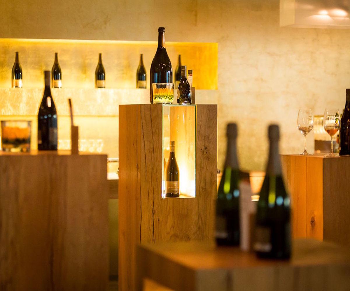  Stilvoller Verkostungsraum mit edler Weinpräsentation auf beleuchteten Holzsäulen und Flaschenregal im Hintergrund