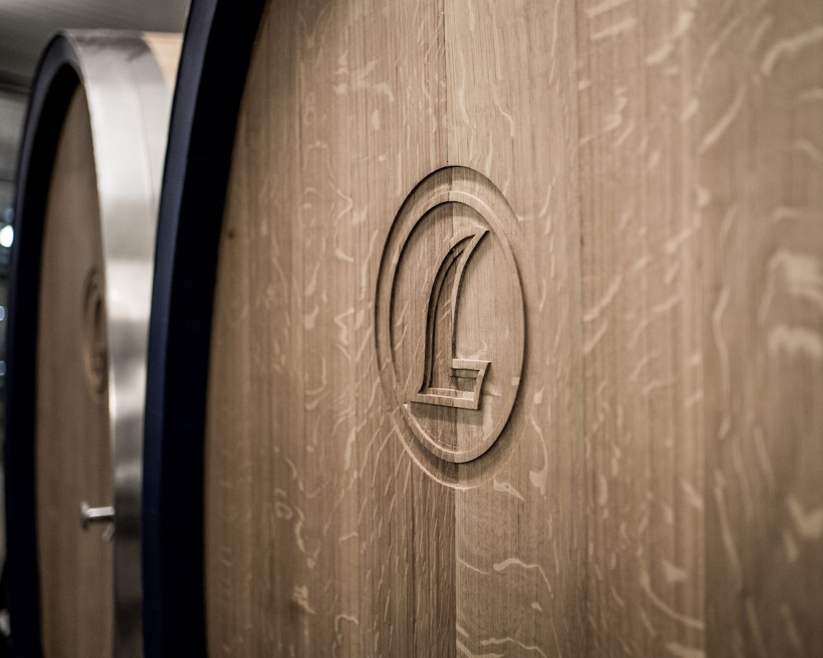  Detailaufnahme eines großen Holzfasses mit eingraviertem Logo auf der Vorderseite, vermutlich in einem Weinkeller