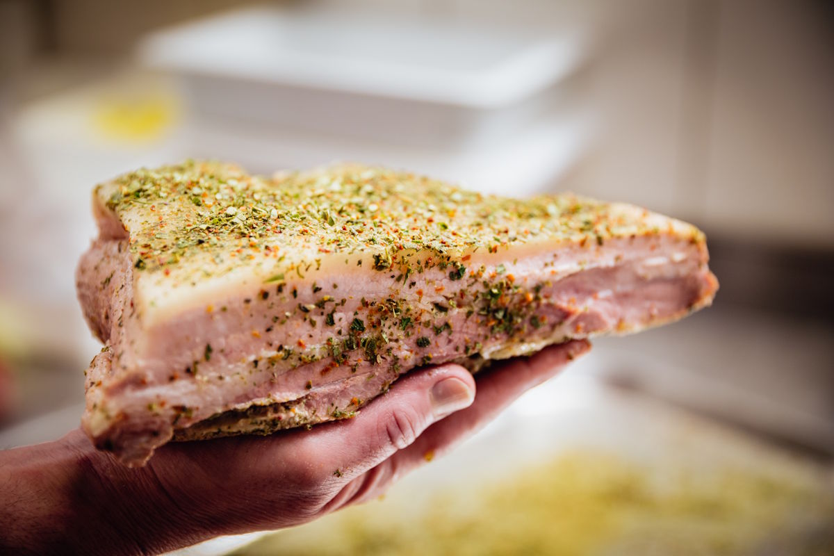 Ein Stück roher Schweinebauch mit Gewürzkruste wird in der Hand gehalten – hochwertige Fleischzubereitung mit Kräutern und Gewürzen als Vorbereitung für Reifung oder Verarbeitung