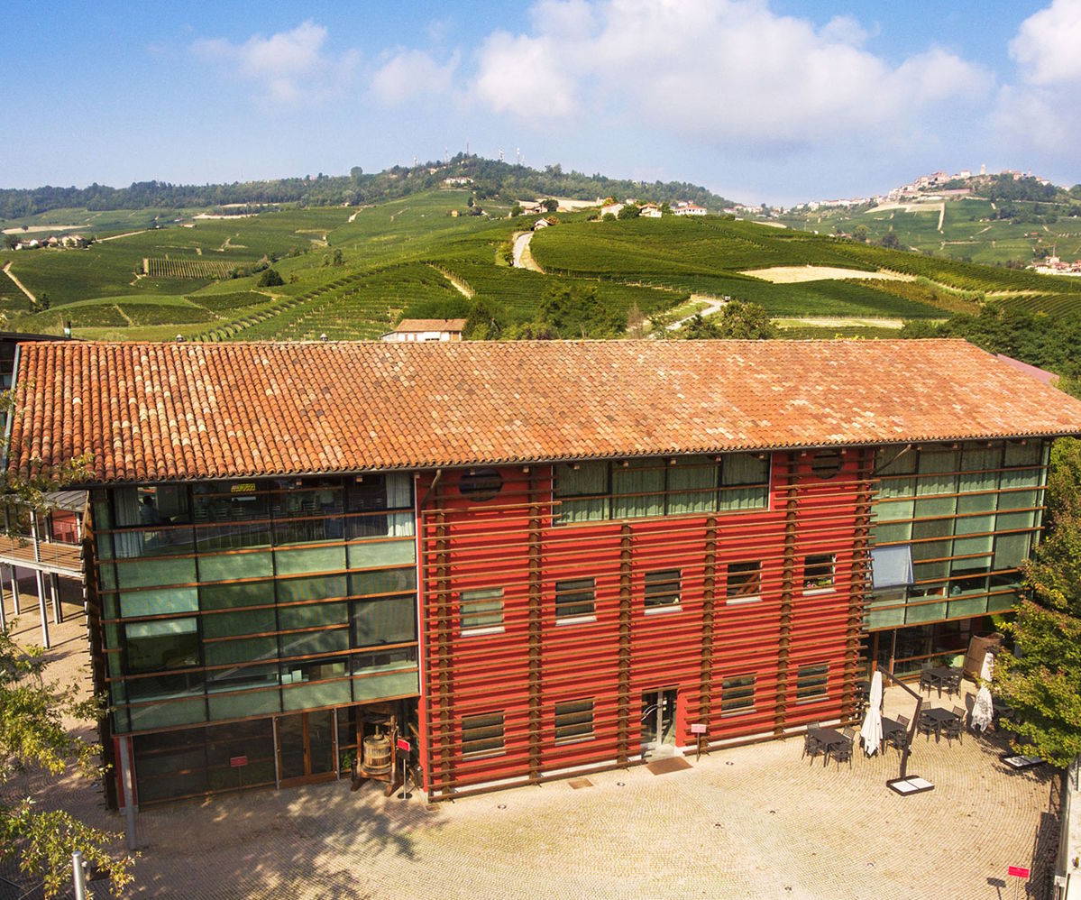 Modernes Weingutsgebäude mit Ziegeldach und roter Fassade vor weitläufiger Hügellandschaft mit Weinbergen