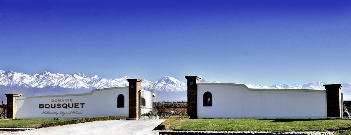 Weißes Eingangsportal der Domaine Bousquet mit Blick auf schneebedeckte Andengipfel unter blauem Himmel.