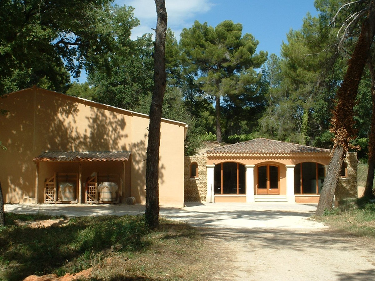 Mediterranes Weingutsgebäude mit ockerfarbener Fassade und Rundbogenfenstern, umgeben von Pinien und Wald.