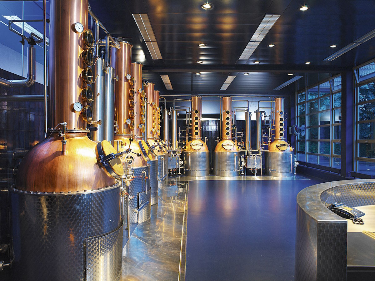 Innenaufnahme einer modernen Destillerie mit glänzenden kupfernen Brennblasen und Edelstahltanks – professionelle Destillationsanlage für die Herstellung von Spirituosen