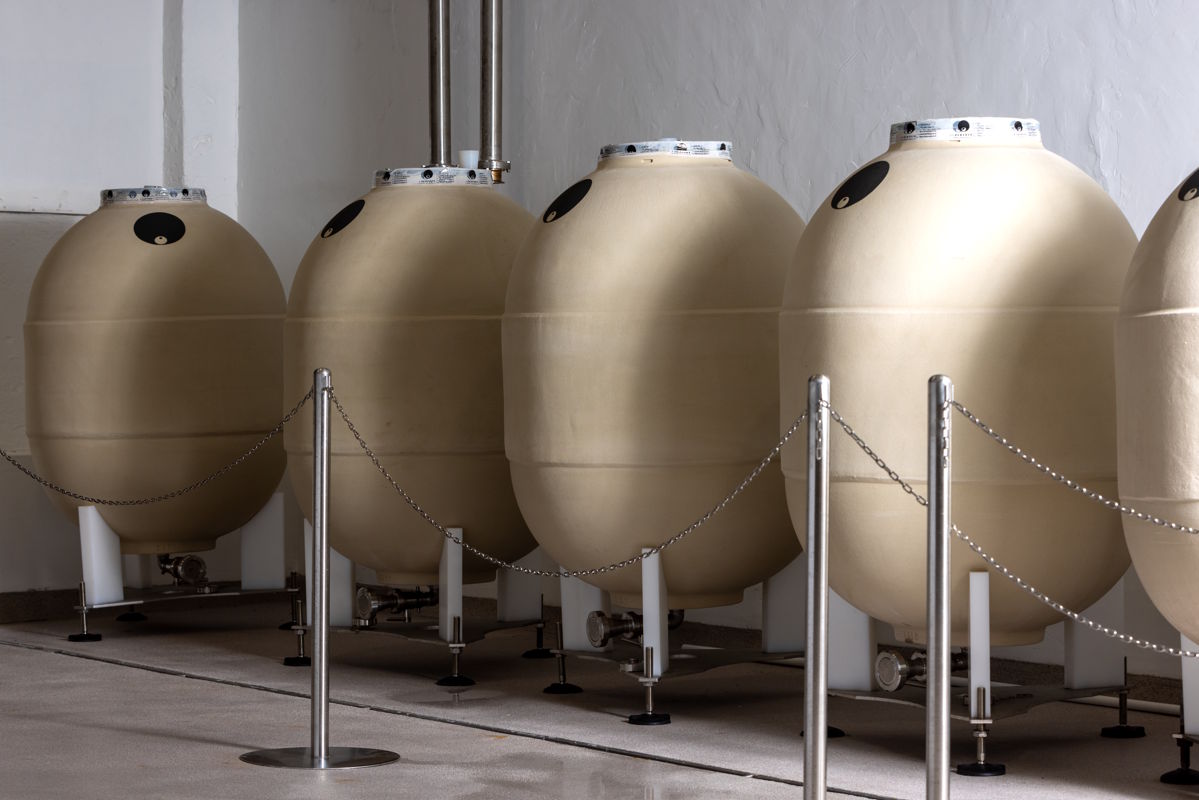 Moderne eiförmige Gärbehälter aus Keramik oder Beton stehen in einer Reihe in einem Weinkeller, durch Absperrungen gesichert.