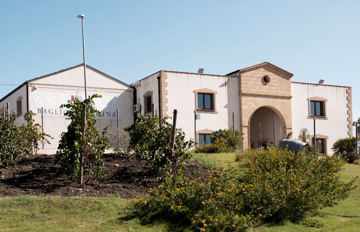 Mediterranes Weingut mit heller Fassade, rundem Torbogen und gepflegtem Garten im Vordergrund unter blauem Himmel