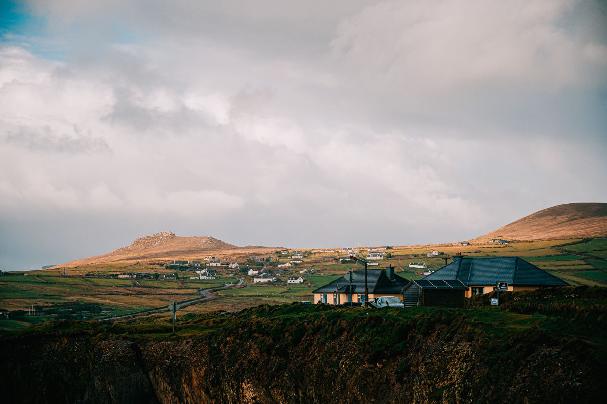 Weitläufige Küstenlandschaft mit einem kleinen Dorf aus verstreuten Häusern und Hütten, eingebettet in grüne Hügel.