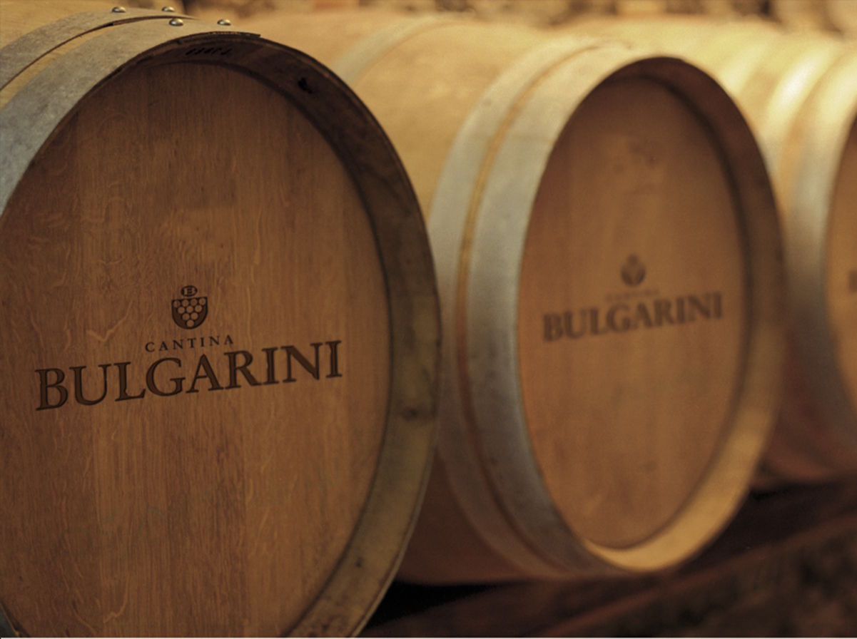 Holzfasslager der Cantina Bulgarini – Tradition und Qualität im Ausbau Nahaufnahme von Holzfässern mit dem Logo und Schriftzug der Cantina Bulgarini in einem stimmungsvoll beleuchteten Weinkeller