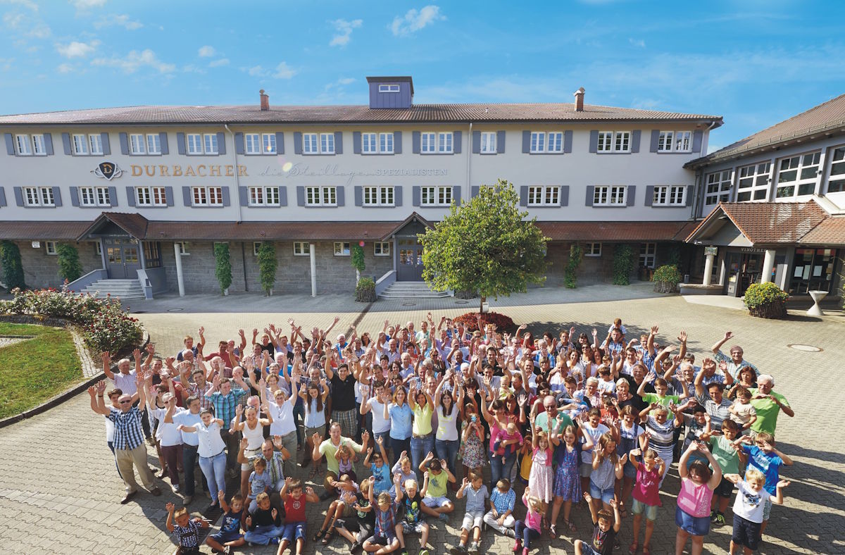  Große Gruppe fröhlicher Menschen vor dem Gebäude der Durbacher Winzergenossenschaft an einem sonnigen Tag