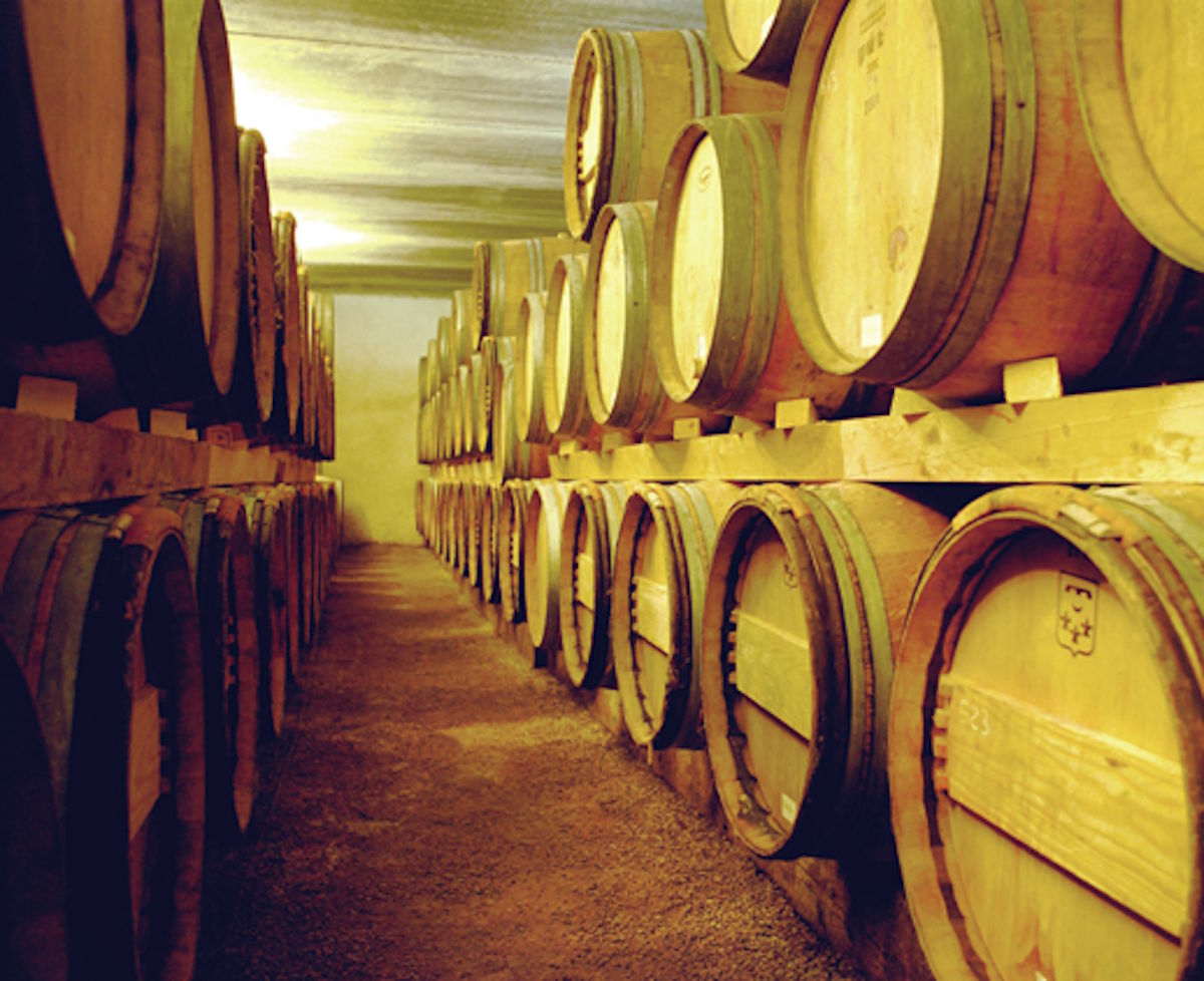 Traditioneller Weinkeller mit gestapelten Holzfässern in zwei Reihen unter gedämpfter Beleuchtung.