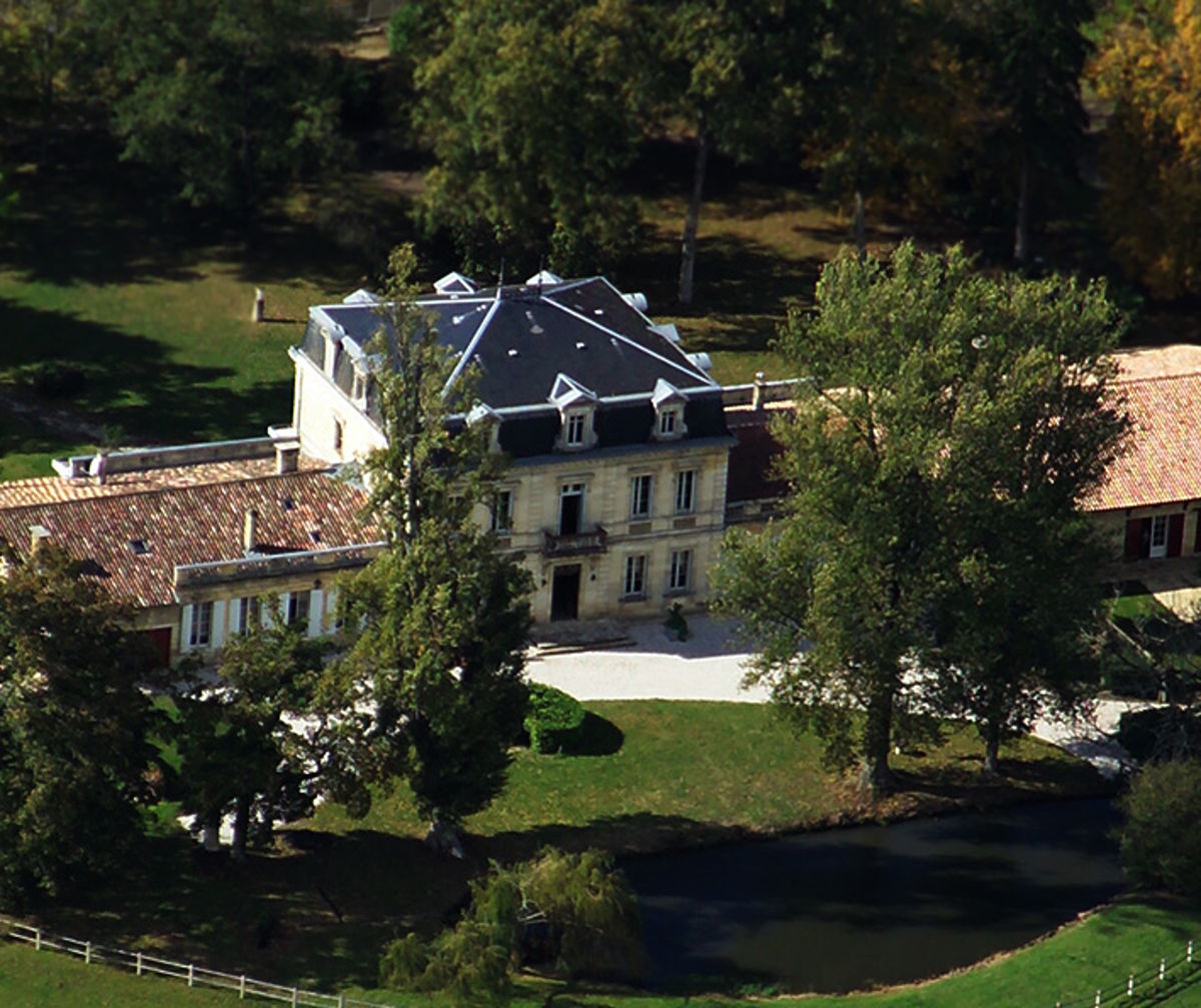 Luftaufnahme eines eleganten Weinguts mit Herrenhaus, Nebengebäuden, altem Baumbestand und einem kleinen Teich im parkähnlichen Gelände.