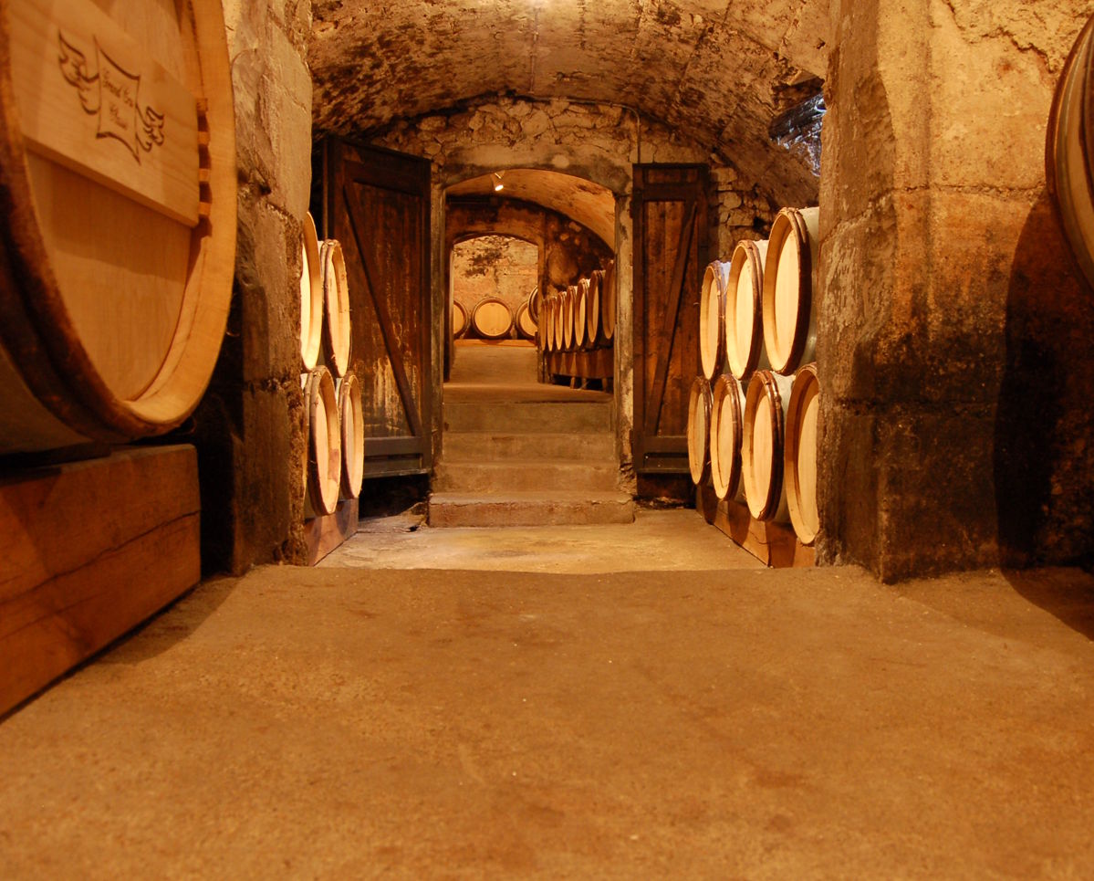 Historischer Weinkeller mit Gewölbedecke und gestapelten Barriquefässern aus Holz entlang der Steinwände.