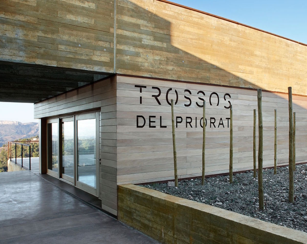 Modernes Weingutgebäude mit klaren Linien, Holz- und Betonfassade, der Aufschrift „Trossos del Priorat“ und Blick auf die umliegende Landschaft.