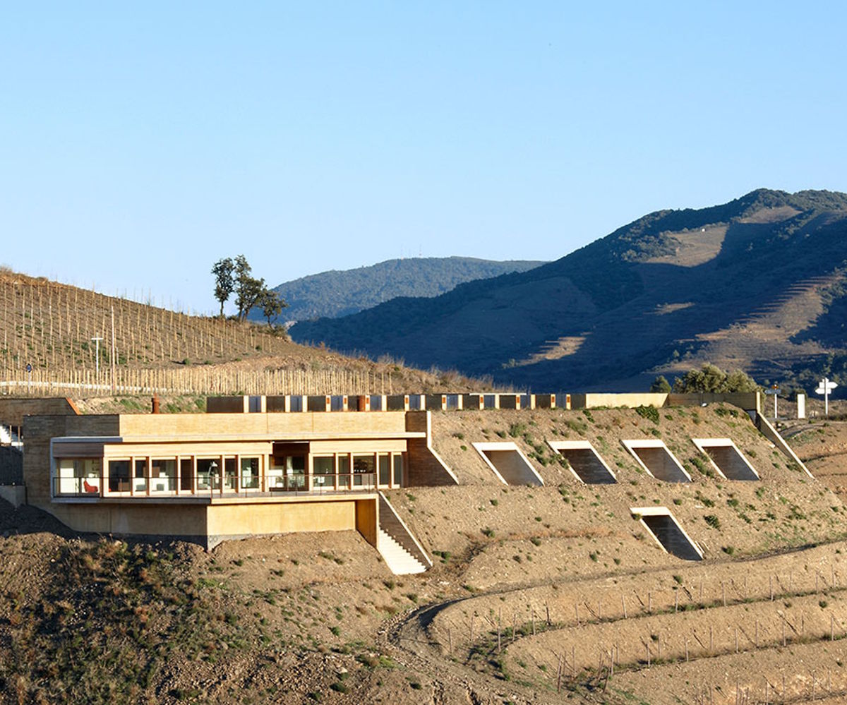 Modernes, terrassiertes Weingut in Hanglage mit kubischer Architektur, eingebettet in eine karge Landschaft mit Blick auf bewaldete Berge.