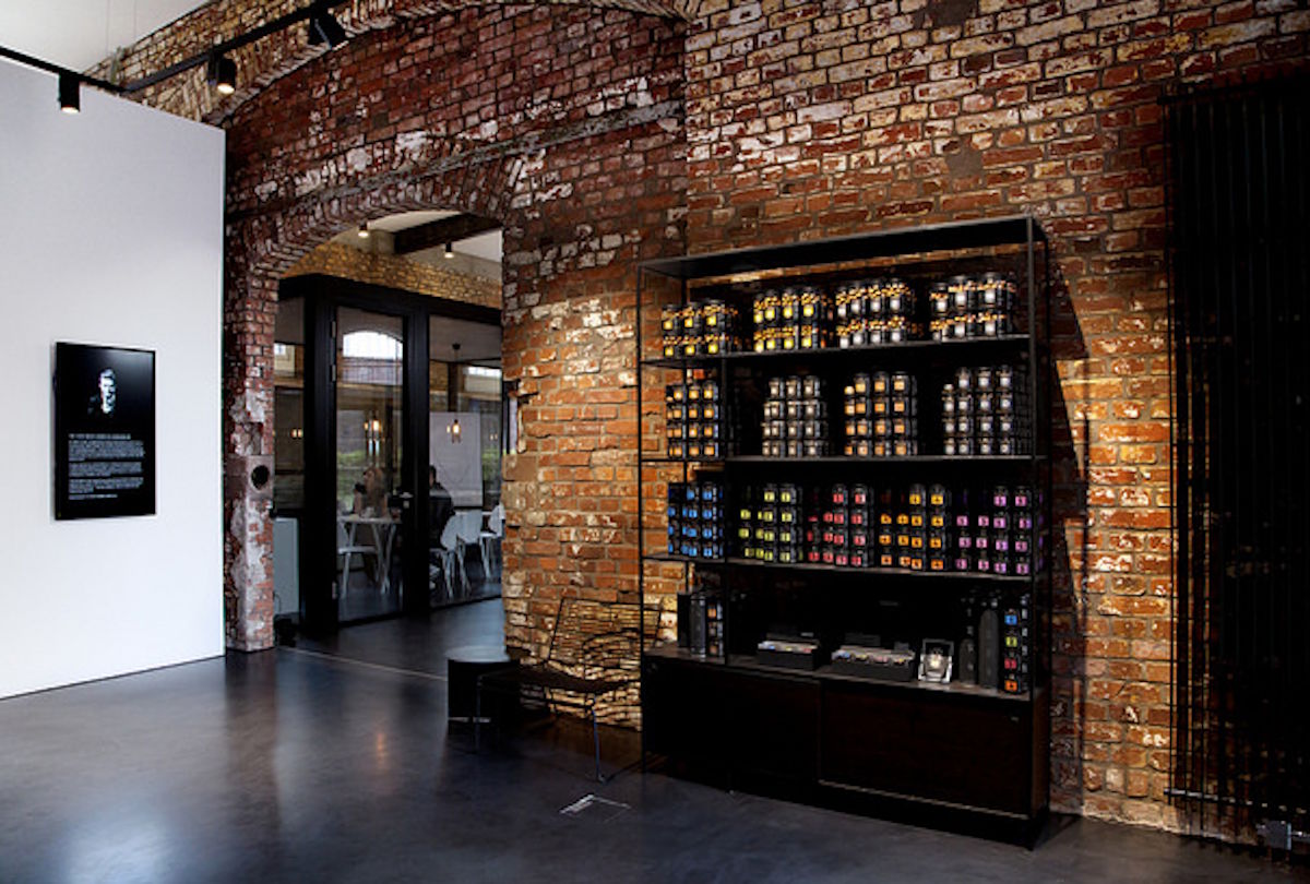 Innenaufnahme eines stilvoll gestalteten Verkaufsraums mit offener Ziegelwand und modernem Bodenbelag, in dem ein Regal mit sorgfältig arrangierten Gläsern und Dosen verschiedener Feinkostprodukte steht