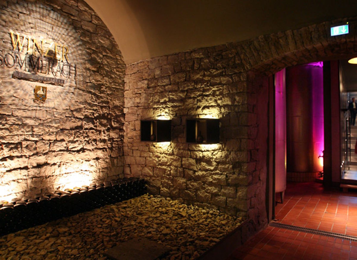  Stimmungsvoll beleuchteter Eingangsbereich eines Weinkellers mit Natursteinwand, eingelassenen Leuchten und dekorativem Flaschenlager