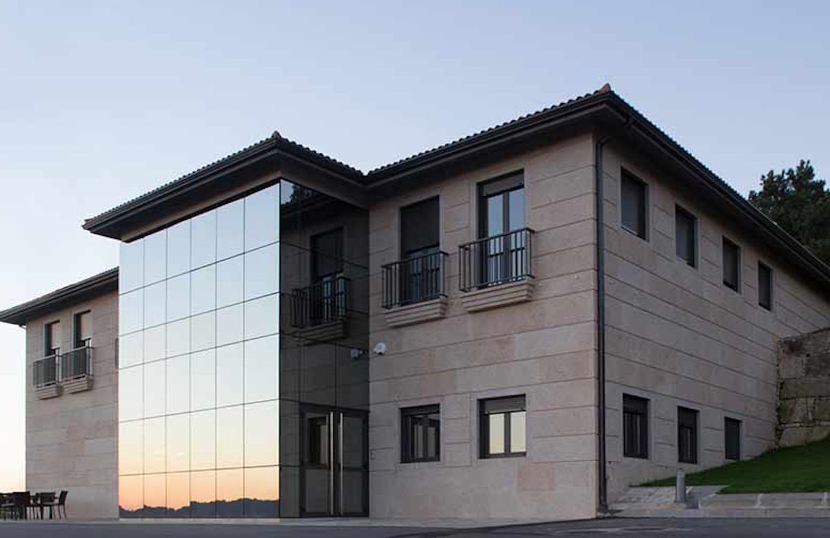 Modernes Weingutsgebäude mit Natursteinfassade und großem verglasten Eingangsbereich, im Abendlicht spiegelnd