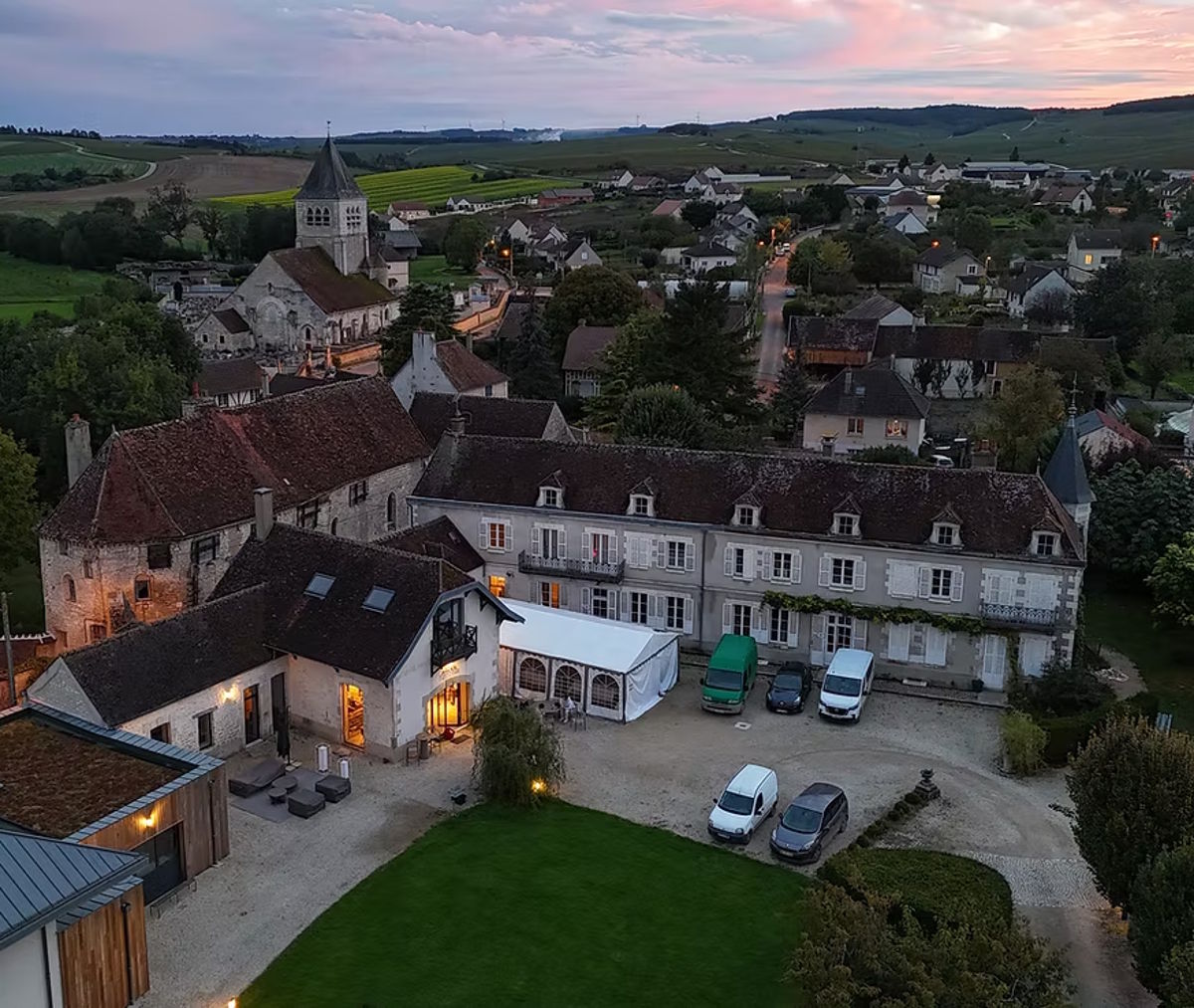 Historisches Weingut mit Innenhof in einem französischen Dorf bei Sonnenuntergang, umgeben von Weinbergen und Landschaft.