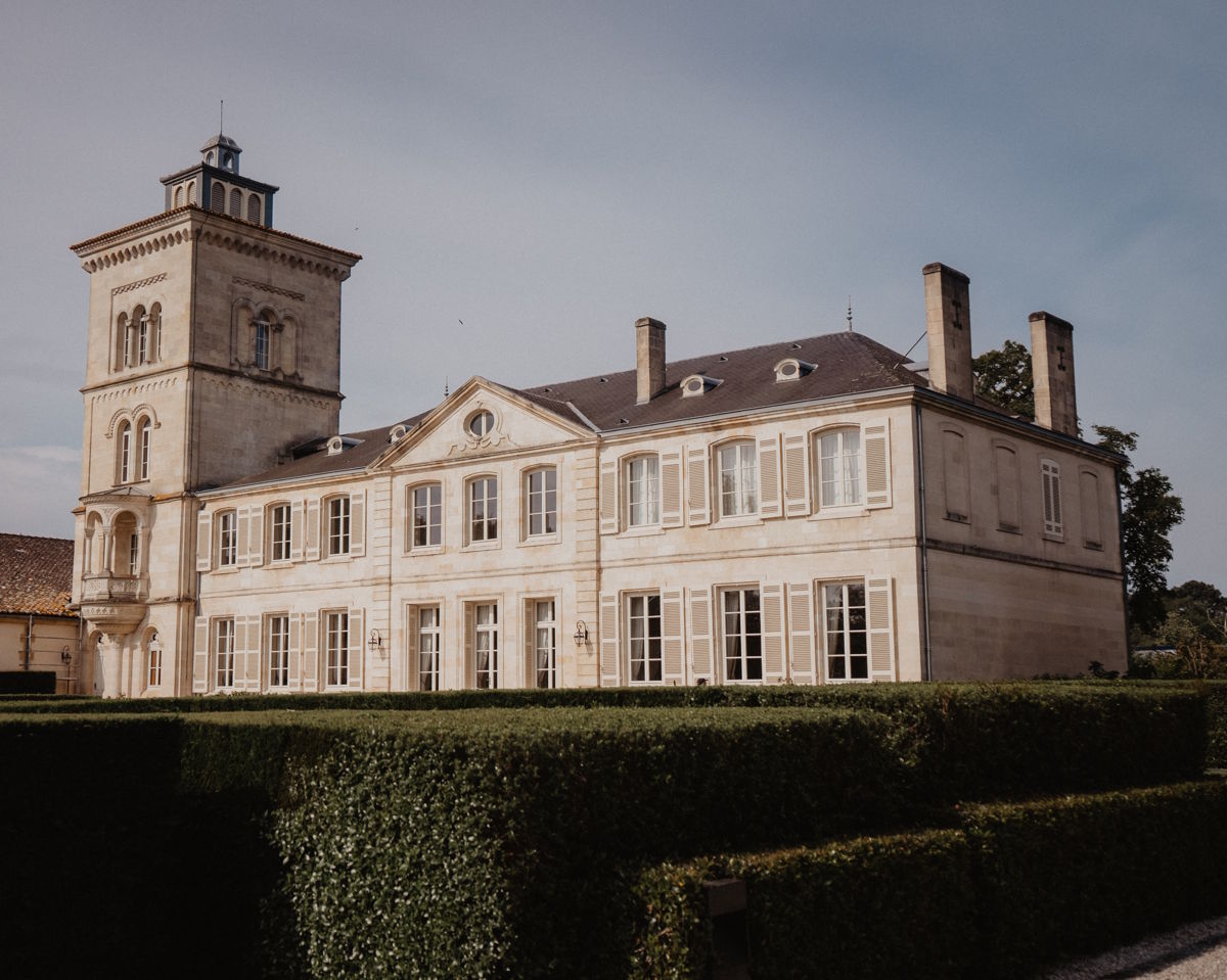 Helles, mehrstöckiges Herrenhaus mit Turm, symmetrischer Fassade und gepflegter Gartenanlage im Vordergrund.