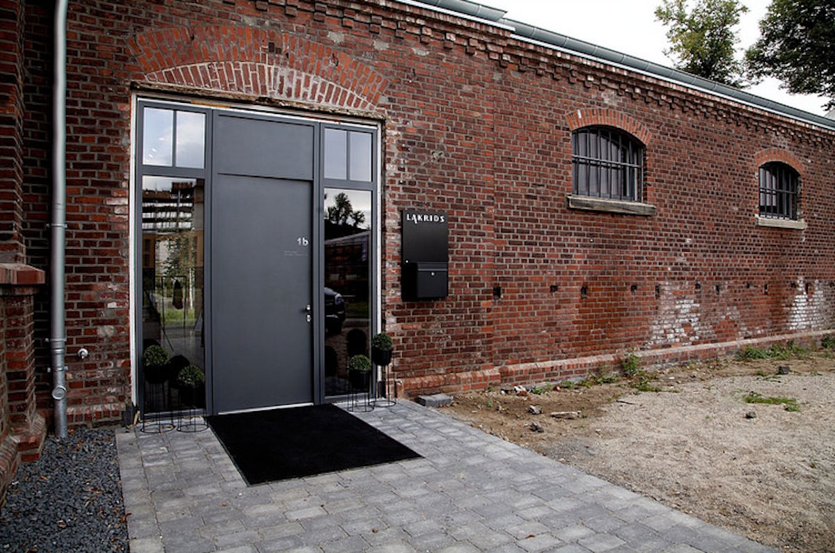 Roter Backsteinbau mit moderner grauer Eingangstür und Pflasterweg, Kombination aus historischer Industriearchitektur und zeitgemäßem Design