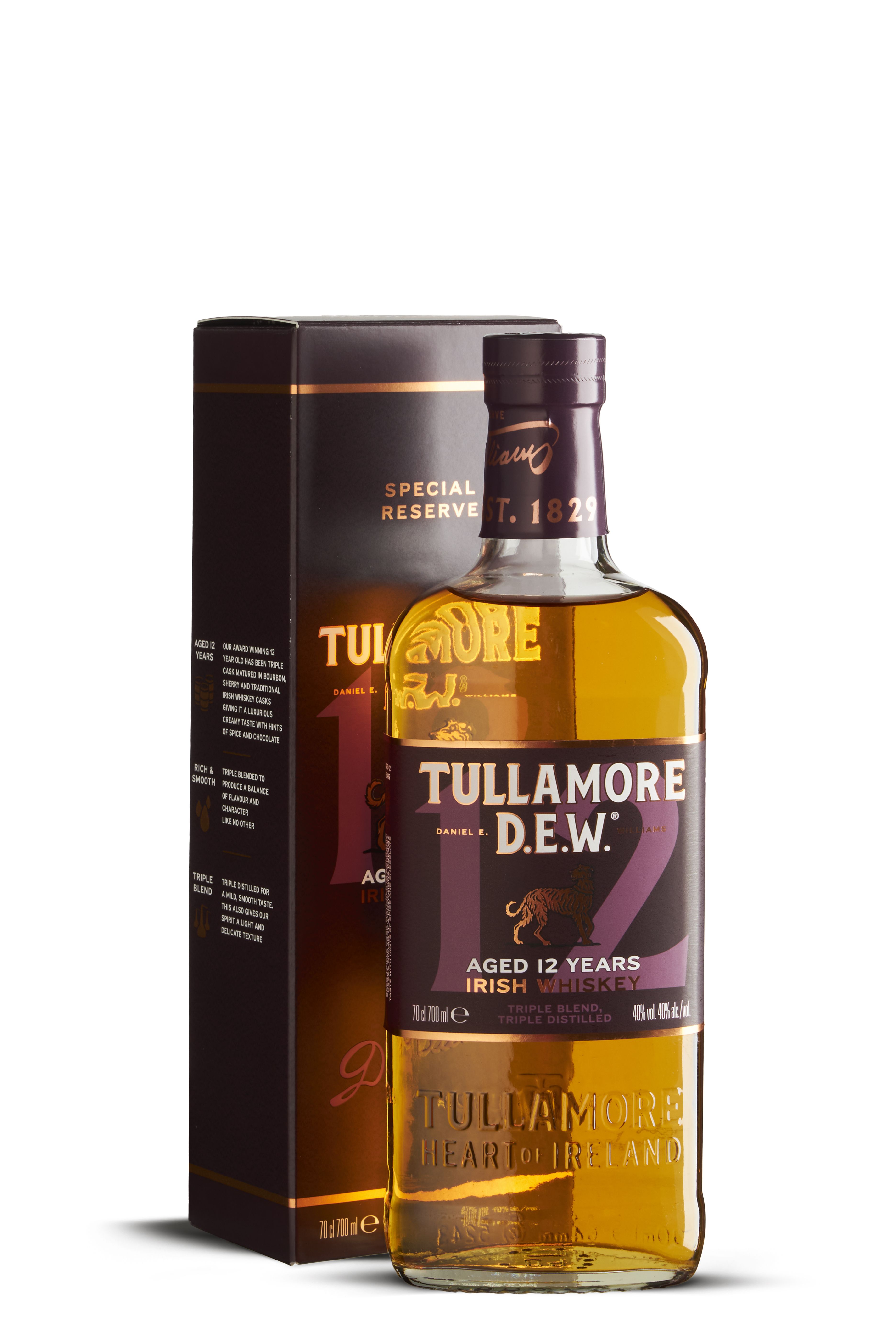Eine Flasche Tullamore D.E.W. 12 Jahre Irish Whiskey mit goldenem Inhalt steht neben der dunkelvioletten Verpackung. Das Etikett zeigt Marke, Alter und dreifache Destillation in elegantem Weiß und Gold.