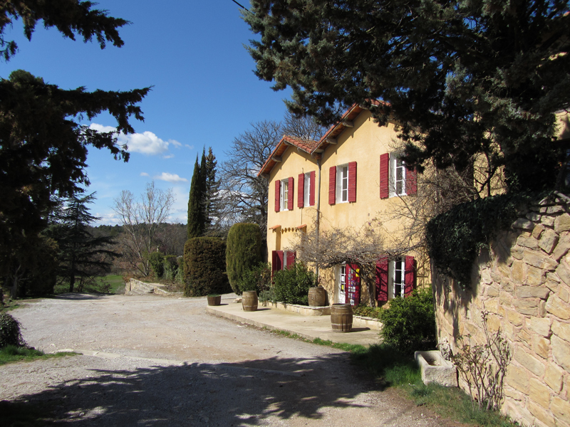 Charmantes Weingut im Landhausstil mit ockerfarbener Fassade und roten Fensterläden inmitten südfranzösischer Landschaft.
