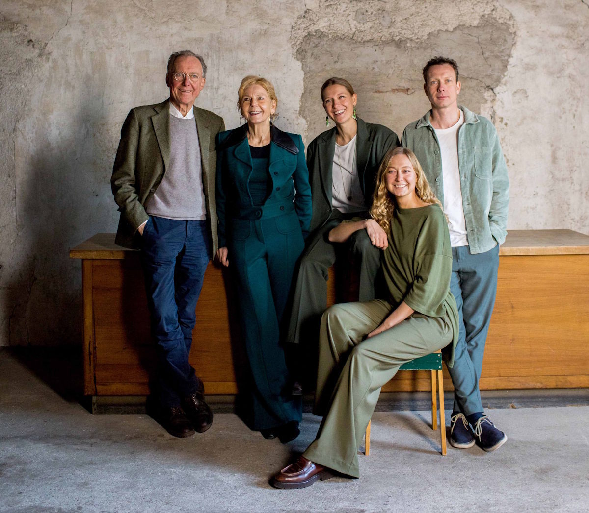  Fünf Personen unterschiedlichen Alters posieren entspannt und stilvoll gekleidet vor einer rauen Steinwand, familiäre und harmonische Atmosphäre