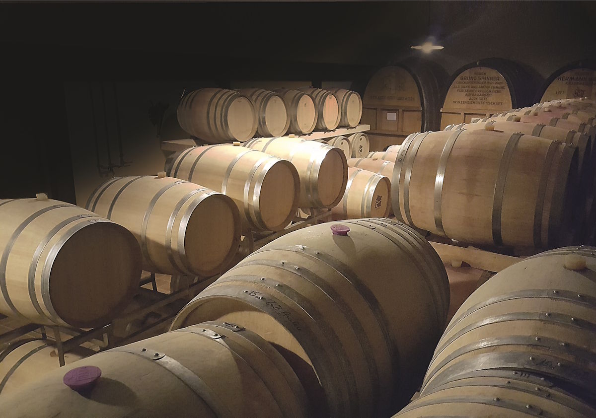 Weinkeller mit zahlreichen gestapelten Holzfässern in gedämpftem Licht, die zur Reifung von Wein dienen
