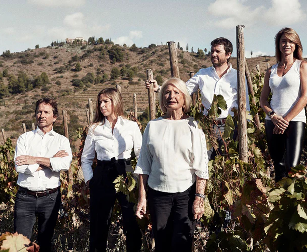 Fünf Personen stehen selbstbewusst in einem Weinberg mit herbstlich gefärbten Reben, im Hintergrund eine hügelige Landschaft mit einem Gebäude auf dem Gipfel.