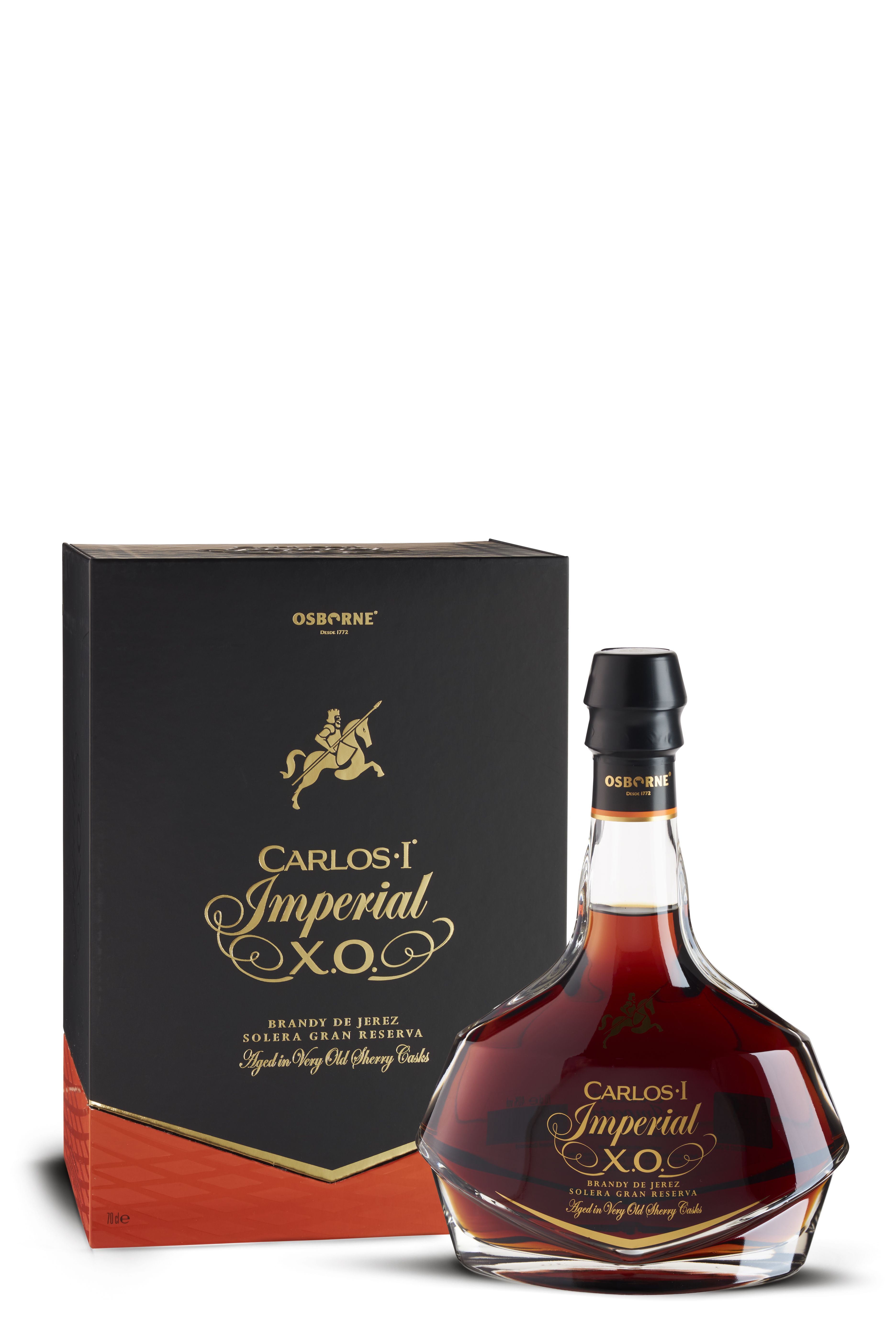 Elegante Flasche Carlos I Imperial X.O. Brandy mit geschwungener Form und goldener Schrift auf dunklem Glas. Daneben eine schwarze Geschenkbox mit Reitermotiv und goldroter Verzierung. Die Flüssigkeit zeigt ein tiefes Mahagonibraun.