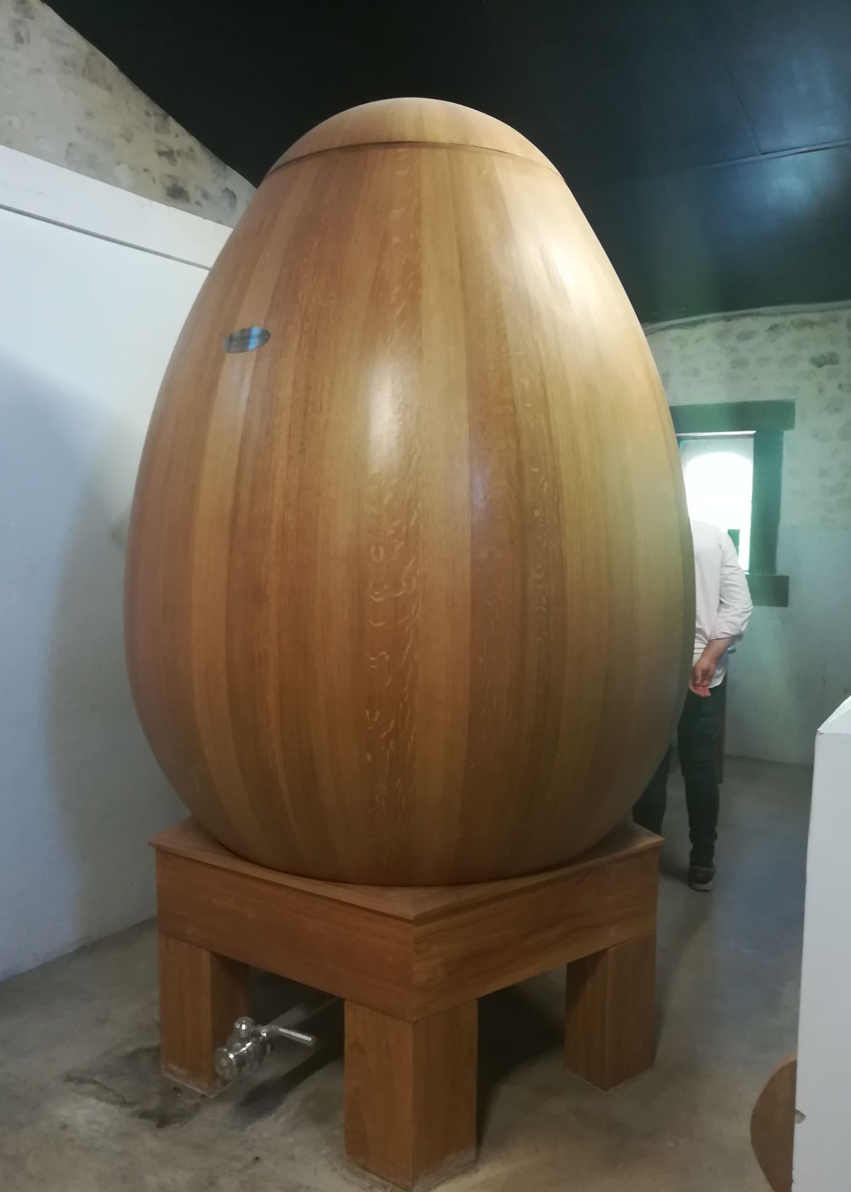 Großes, eiförmiges Holzfass auf einem stabilen Holzgestell in einem modernen Verkostungs- oder Produktionsraum – genutzt für die Reifung von Wein oder Spirituosen in einer innovativen Fassform