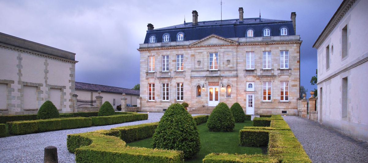 Prächtiges Weingut-Herrenhaus im klassizistischen Stil mit gepflegtem, symmetrisch angelegtem Garten im Vordergrund und dramatischem Himmel im Hintergrund.