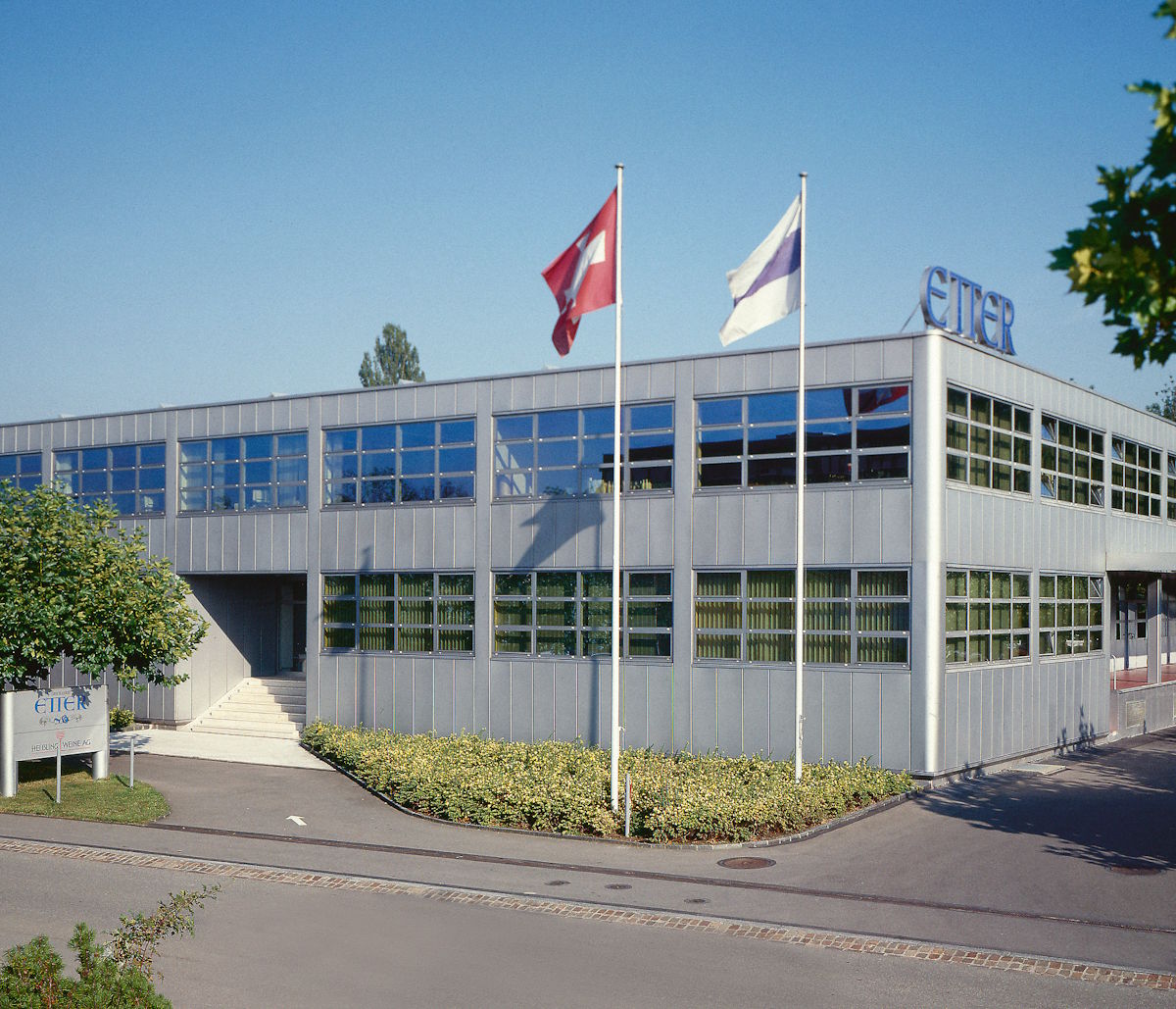 Außenansicht eines modernen Firmengebäudes mit großflächigen Fenstern und Schweizer Flagge – Verwaltungs- und Produktionsstandort der Spirituosenmanufaktur Etter