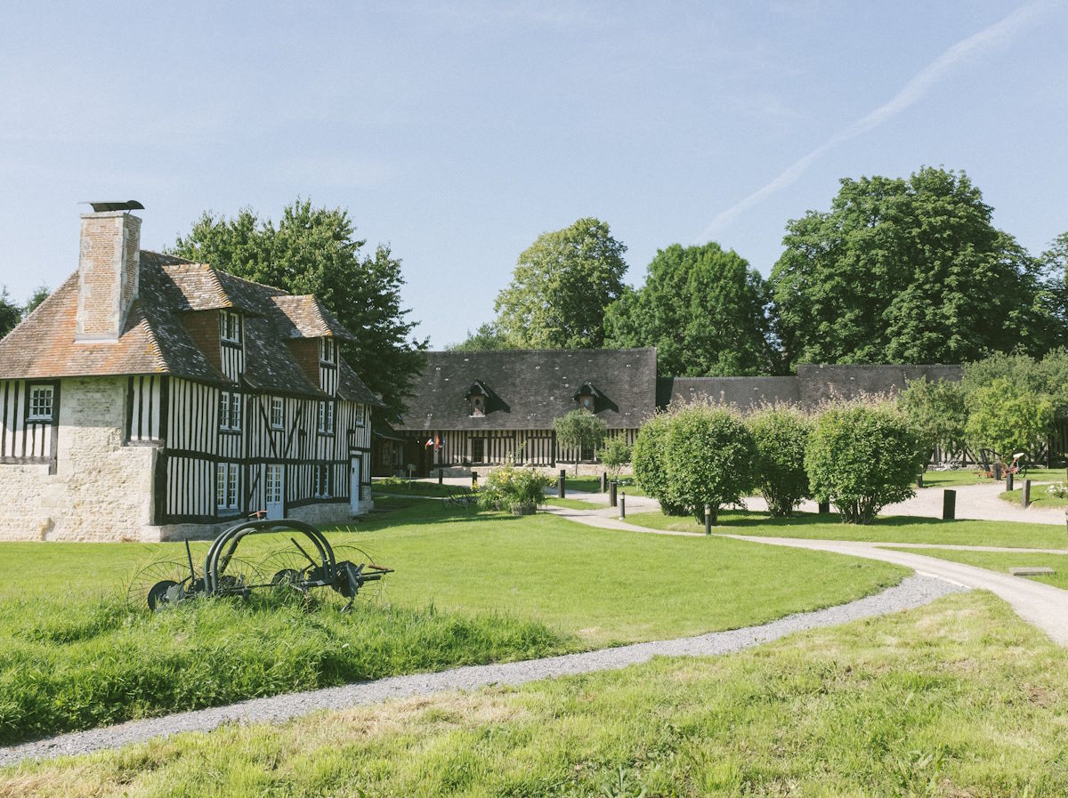 Traditionelles Fachwerkhaus mit Steinmauern und Schornstein auf einem gepflegten, grünen Anwesen mit alten Bäumen und Kieswegen – ländliche Idylle und historische Architektur bei sonnigem Wetter